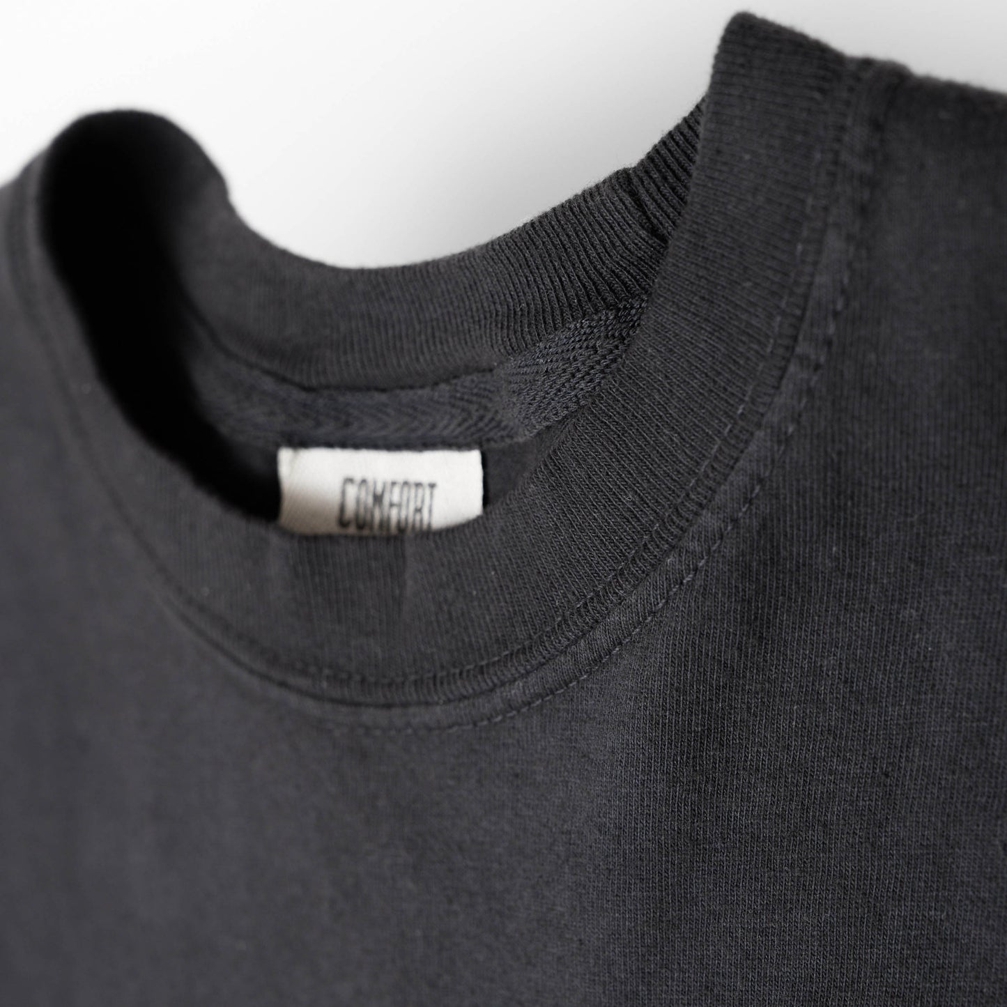 Close-up of view of the crew neck on a black shirt with a visible label on a white background.