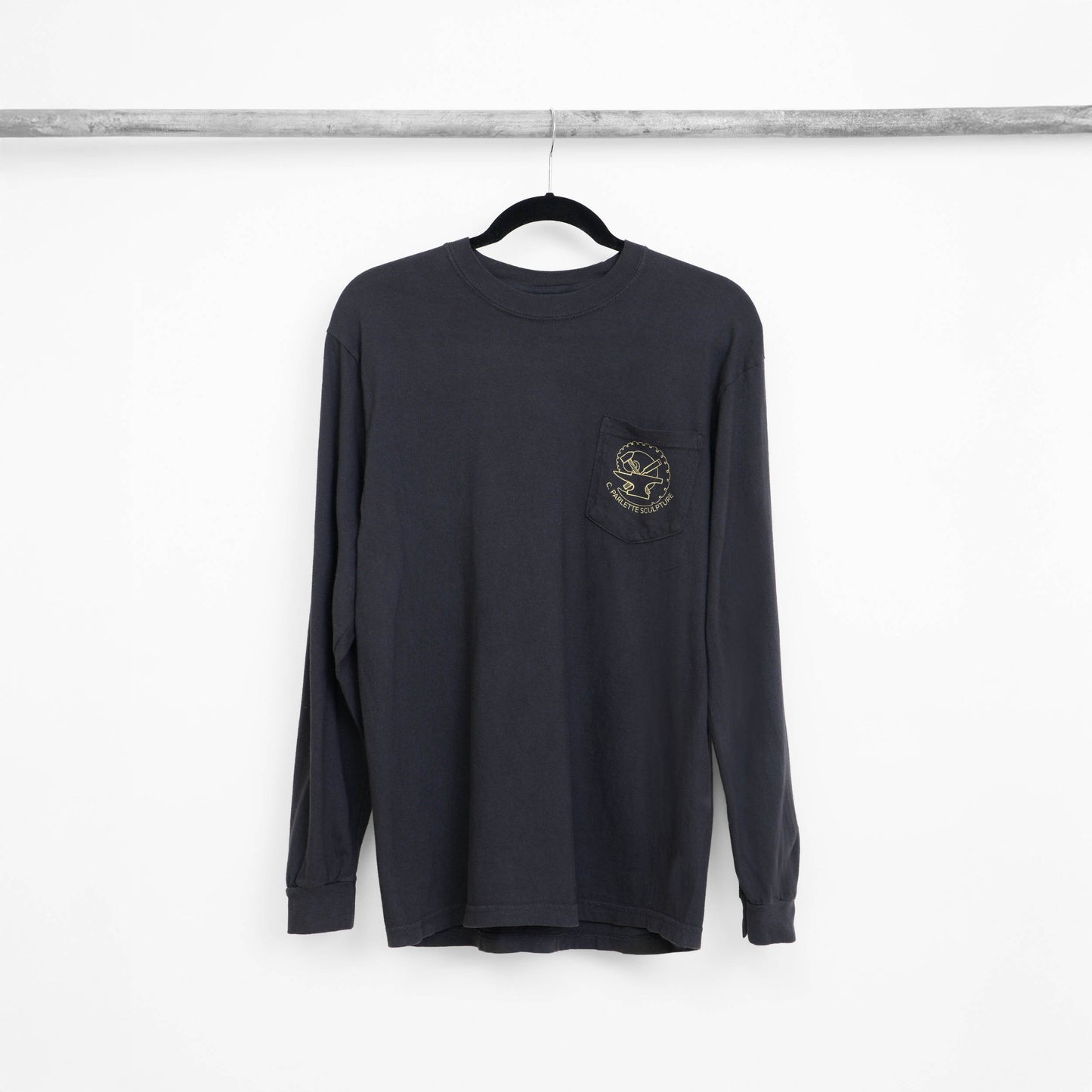 Black long-sleeve, crew neck shirt with a pocket and logo of an anvil with tools against a nautilus shell with the text 'C. Parlette Sculpture' below.