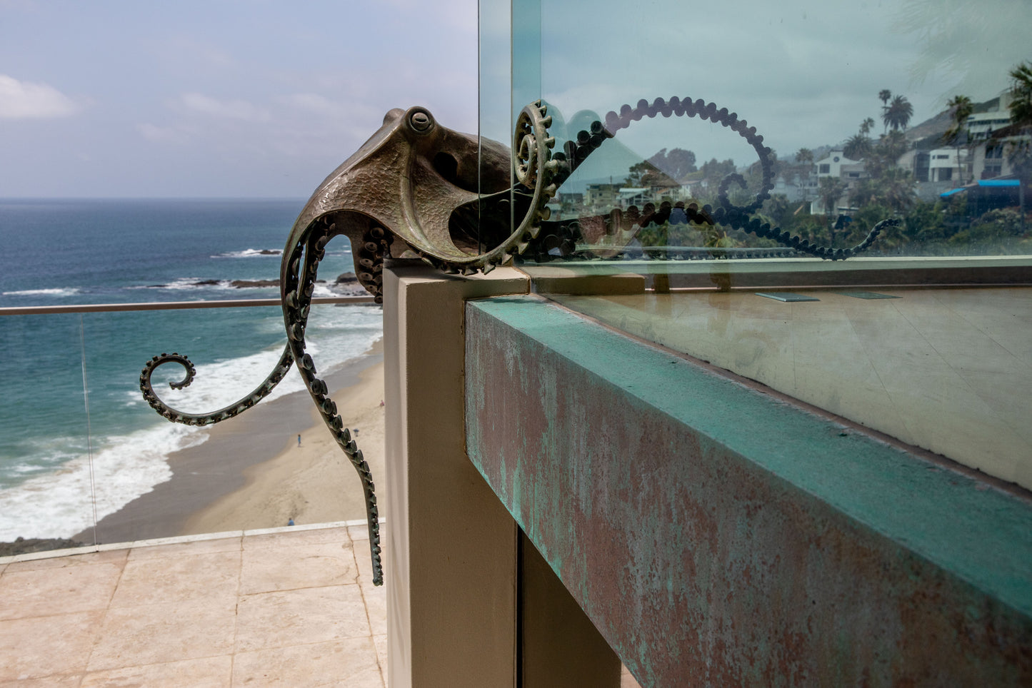 Decorative metal sculpture of an octopus posed as if its crawling on a balcony with ocean view.