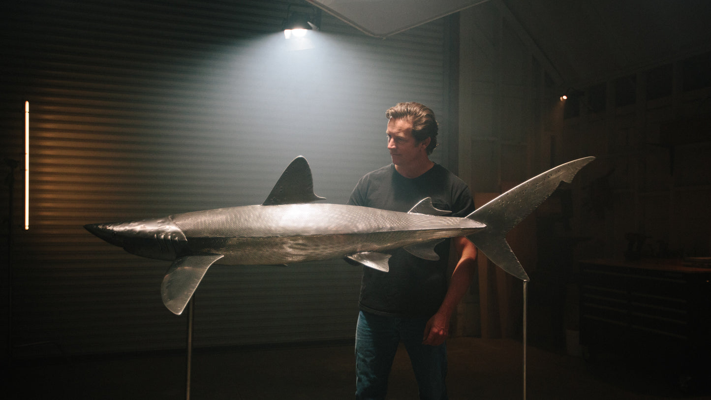 Casey Parlette standing in his studio beside his large metal shark sculpture.
