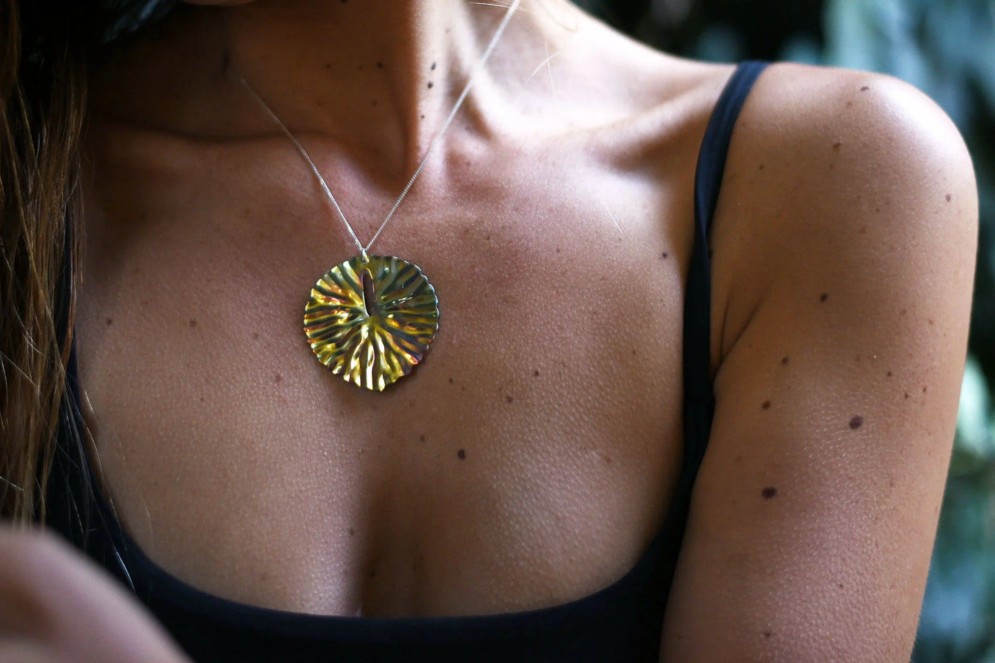 Close-up of a person wearing a necklace with an iridescent lily pad pendant.